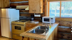 Une cuisine rustique, située dans une cabane en bois, équipée d’une cuisinière, d’un réfrigérateur, d’un four à micro-ondes et d’un évier.