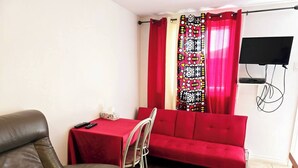 Une pièce comprenant un fauteuil en cuir, un canapé rouge, une petite table avec un boîte de mouchoirs, et un téléviseur fixé au mur.