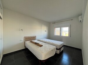 A small, clean room with two single beds, a window with blinds, and a plain white wall. - Seafront Apt Platja dáro (Calonge)