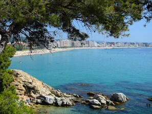 A coastal view with clear blue water, rocky shoreline, and a distant cityscape. - Seafront Apt Platja dáro (Calonge)