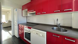 Eine moderne Küche mit roten Schränken, einer Edelstahl-Spüle, einem eingebauten Backofen und einem Geschirrspüler.