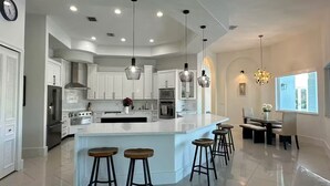 A modern kitchen with white cabinets, a central island with stools, stainless steel appliances, and pendant lighting. - Welcome to Casa Hibiscus, your private tropical escape in Miami! 4-bd, 4-baths (Miami)