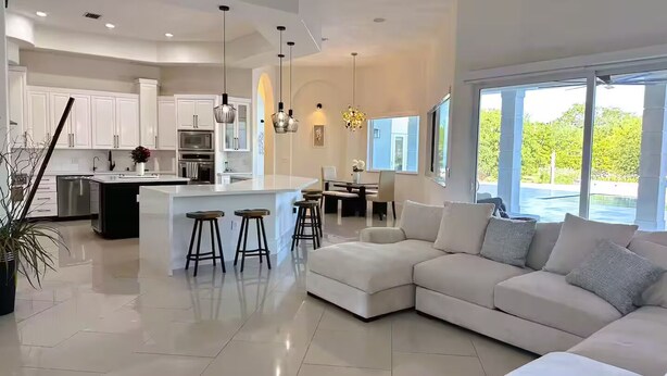 A modern kitchen with white cabinets, a central island with stools, and pendant lighting. - Welcome to Casa Hibiscus, your private tropical escape in Miami! 4-bd, 4-baths (Miami)