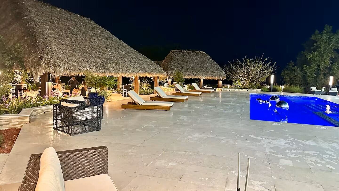 Ein Poolbereich mit Liegestühlen und strohgedeckten Pavillons.