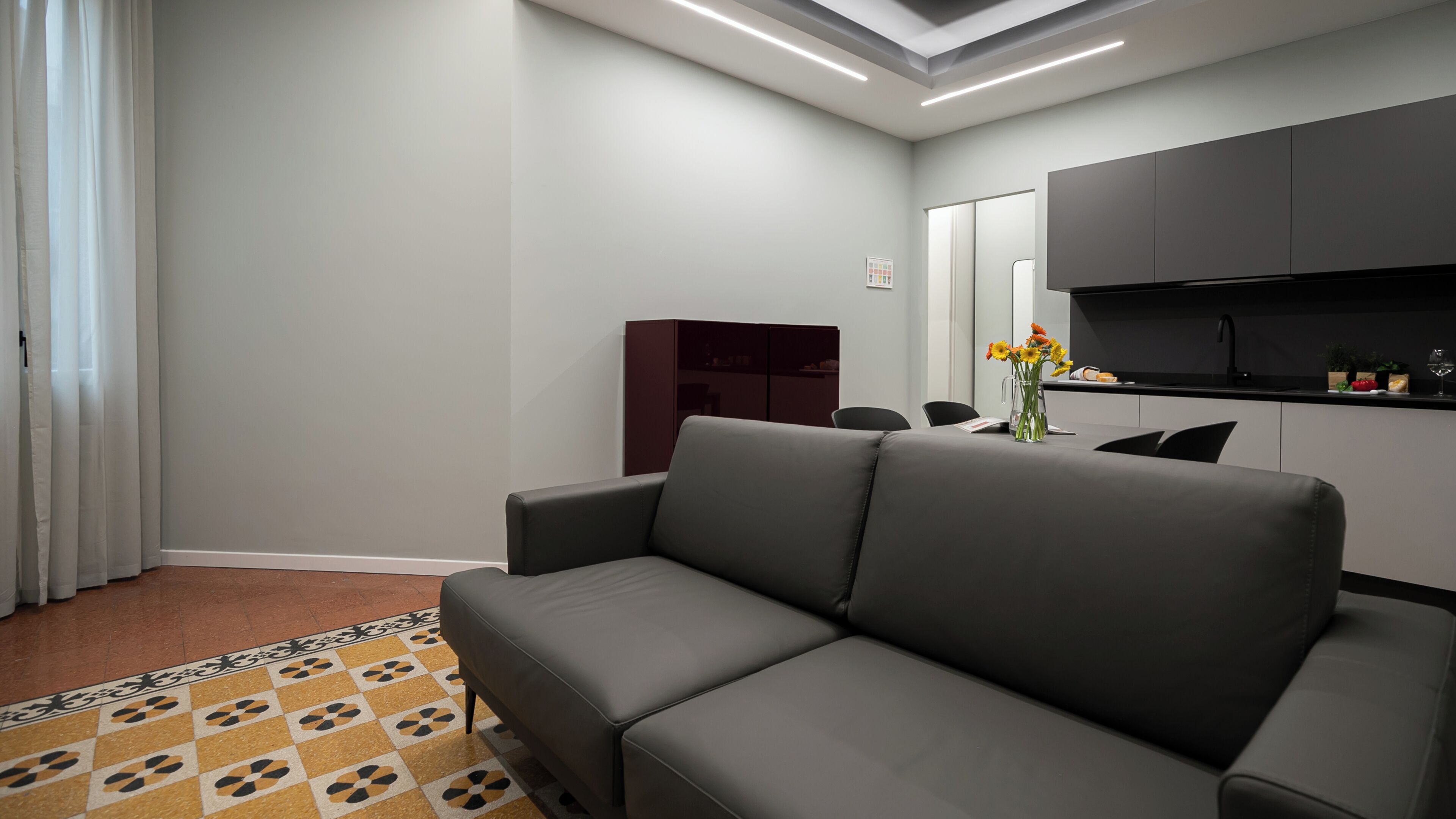 Un salon moderne avec un canapé gris, un coin cuisine doté de meubles sombres et un tapis à motifs.
