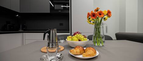 A modern kitchen with a coffee maker, a bowl of fruit, a vase with flowers, and a plate of croissants.