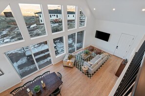 A spacious living area with large windows, a dining table, and a sofa. - Sweetwater Links Lodge | Sleeps 20, Ideal Beach, Arcades, BBQ, Lake Views! (Garden City)