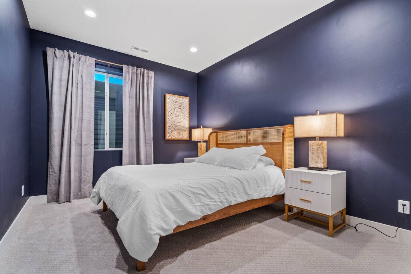 A bedroom with a bed, nightstands, a window with curtains, and a wall-mounted artwork.