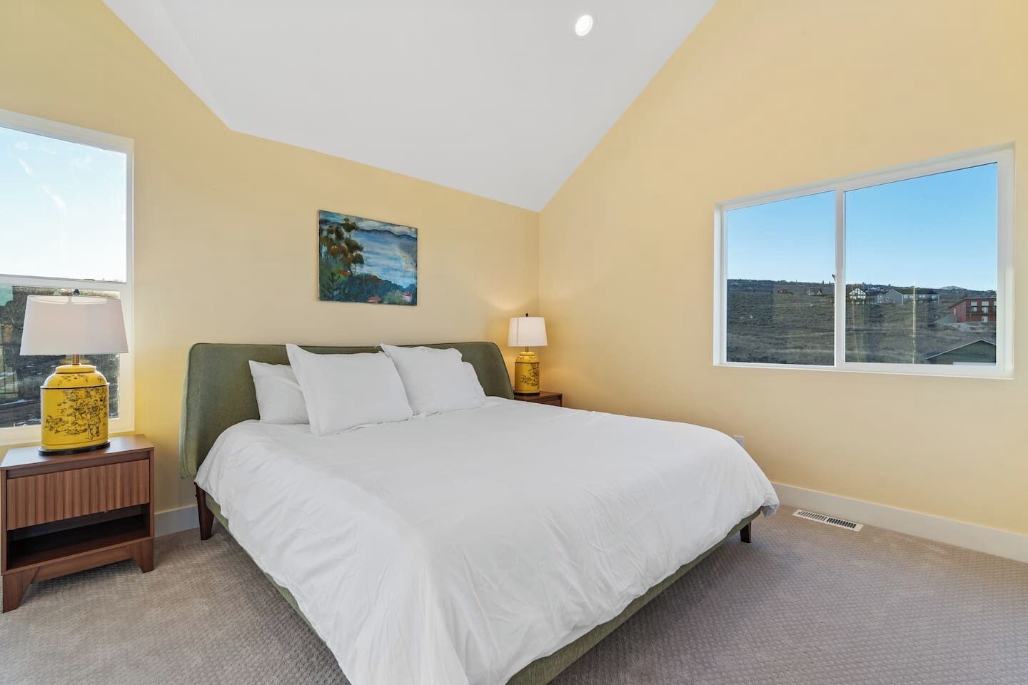 A bedroom with a bed, two bedside tables, a window, and a painting on the wall.