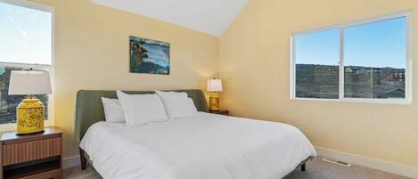 A bedroom with a bed, two bedside tables, a window, and a painting on the wall.