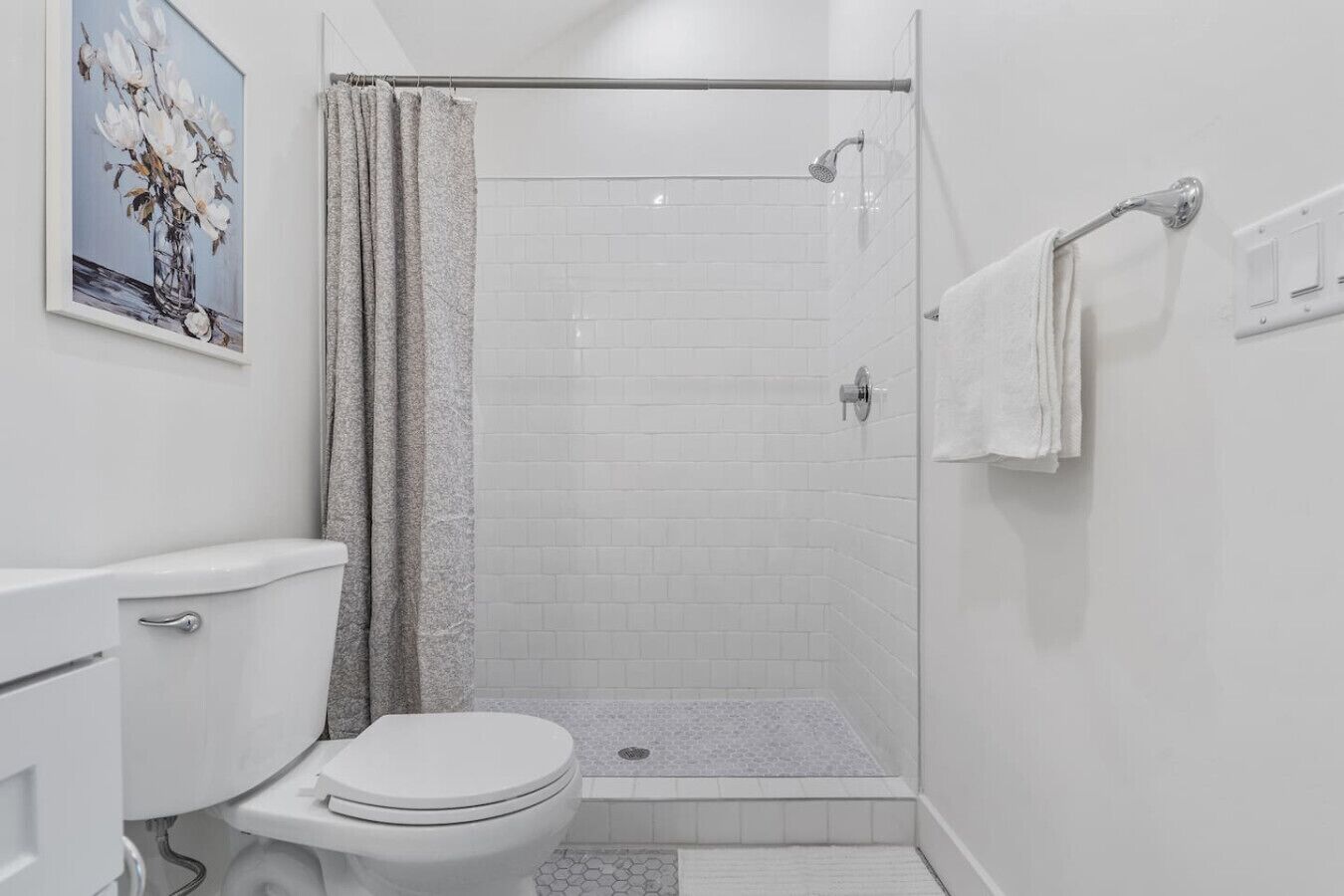 A small, modern bathroom with a white toilet, a shower with a glass door, and a white tiled shower floor.