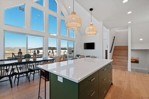 A spacious kitchen with large windows, a central island, and a staircase leading to an upper level. - Sweetwater Links Lodge | Sleeps 20, Ideal Beach, Arcades, BBQ, Lake Views! (Garden City)