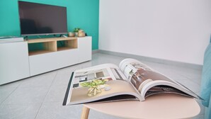 Ett modernt vardagsrum med en platt-TV placerad på en vit TV-bänk, en tidning på ett litet bord och en turkosfärgad accentvägg.
