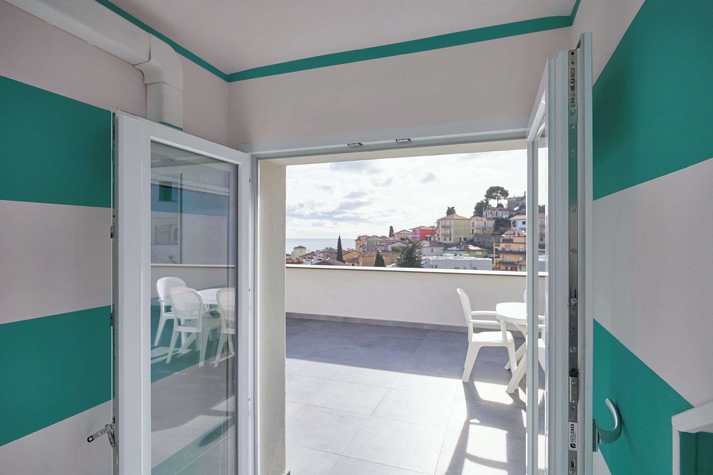 An open sliding glass door leading to an outdoor balcony with white chairs and a table.