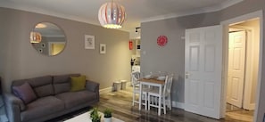 A living room with a sofa, a dining table with chairs, a mirror, and a door leading to another room. - Modern Central 1BDR At St Stephen Green (Dublin 2)
