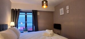 A hotel room with a bed, a lamp, a TV, a window with curtains, and a view of a building outside. - Modern Central 1BDR At St Stephen Green (Dublin 2)