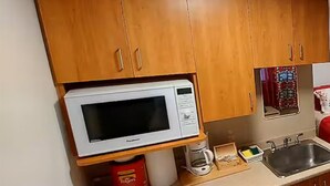 A kitchen with wooden cabinets, a white microwave, a coffee maker, and a sink. - #102 Enjoy your stay (Trois-Rivières)