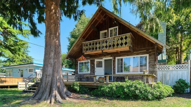 A log cabin with a balcony, surrounded by trees and a small garden.