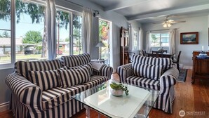 A living room with striped sofas, a glass coffee table, and large windows with curtains.