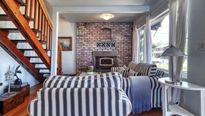 A cozy living room with a brick fireplace, striped sofas, and a wooden staircase.