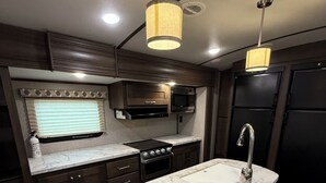 A compact kitchen with dark wood cabinets, a marble countertop, a built-in microwave, and a stainless steel sink. - One bedroom RV next to OWA,restaurants, waterpark, and 15 minutes from beach. (Foley)