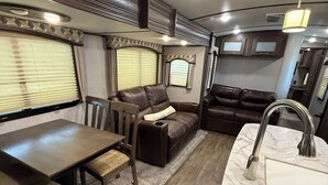 A compact RV interior with a dining area, a seating area with a sofa and ottoman, and a kitchen with a sink and countertop. - One bedroom RV next to OWA,restaurants, waterpark, and 15 minutes from beach. (Foley)