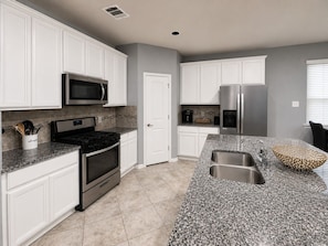 A modern kitchen with white cabinets, a stainless steel refrigerator, a microwave, an oven, and a granite countertop.