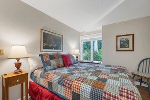 Una camera da letto con un letto grande, due lampade sui comodini, una finestra vista su un paesaggio verde e due quadri appesi al muro.