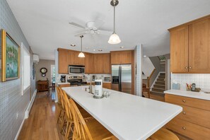 A kitchen with wooden cabinets, a large island, stainless steel appliances, and a ceiling fan. - Lakefront Retreat Near Pleasant Mountain (Bridgton)