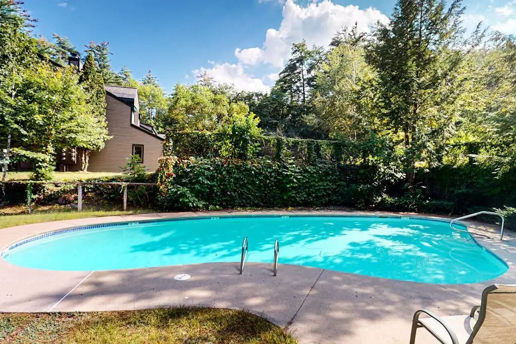Ein Schwimmbad mit einer Holzterrasse und einem Haus im Hintergrund.