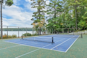 A tennis court with a net, surrounded by trees and a body of water. - Lakefront Retreat Near Pleasant Mountain (Bridgton)