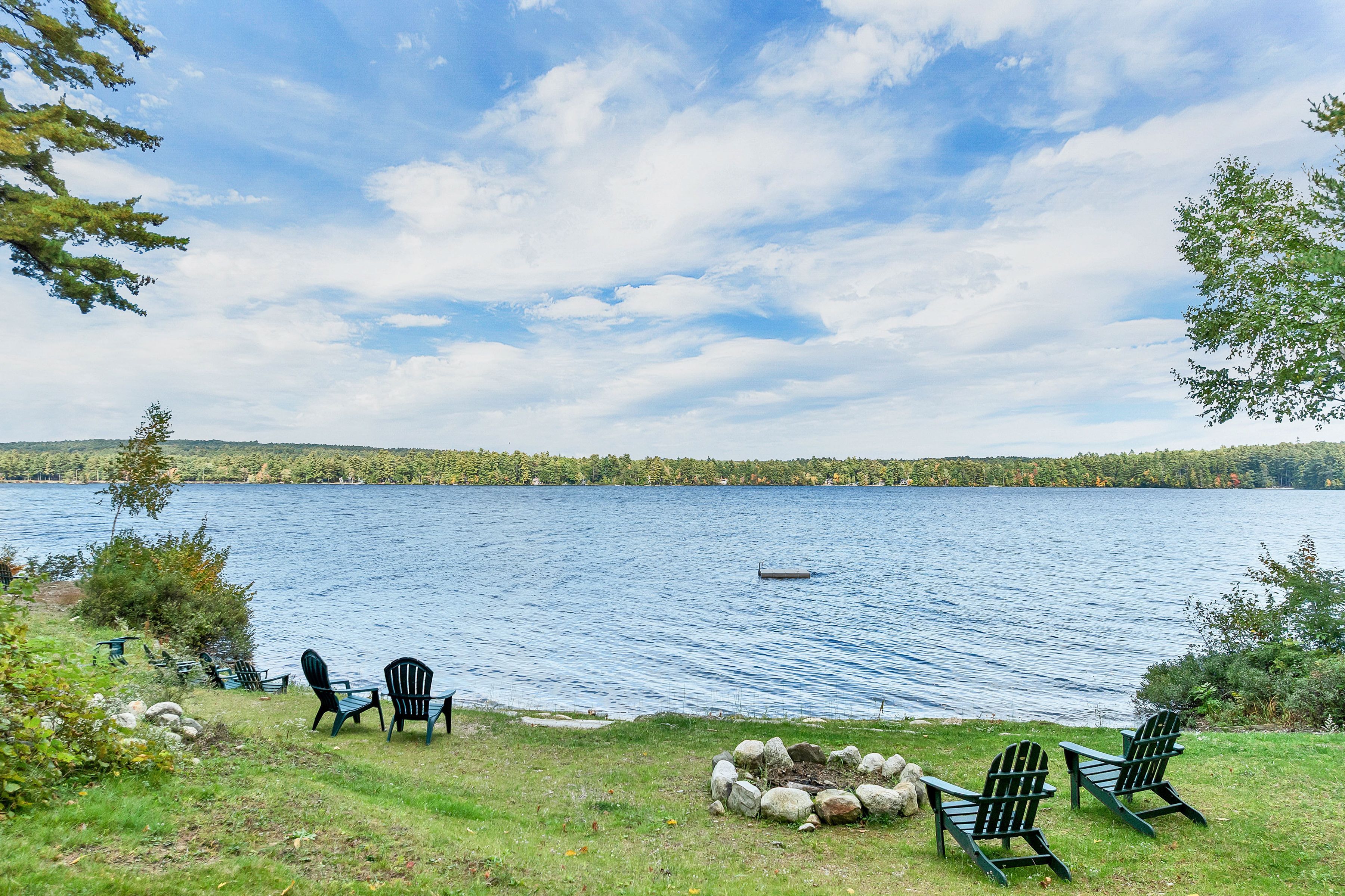 A lakeside view with chairs and a fire pit.