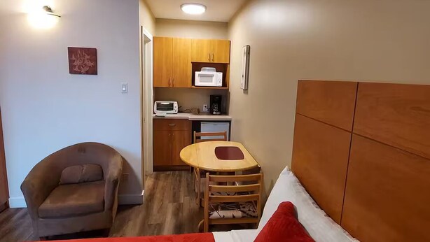A compact room with a bed, a chair, a small table, and a kitchenette. - #110 Enjoy your stay (Trois-Rivières)