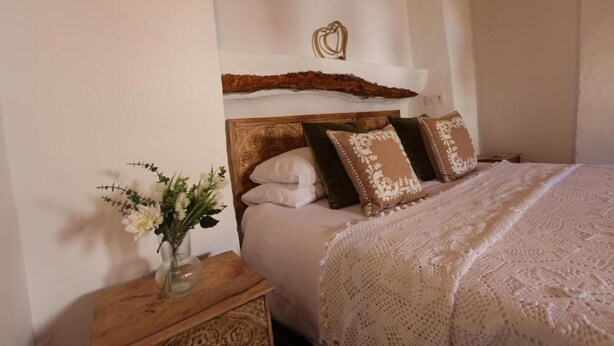 A bedroom with a wooden headboard, a bed with a white and brown patterned bedspread, and a nightstand with a vase of flowers. - Apartment Sleeps 4 Alhama de Granada Town Centre (Alhama de Granada)