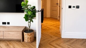 A modern living room with a flat-screen TV, a wooden cabinet, a potted plant, and a herringbone-patterned floor. - East Parade Collection, The Penthouse (North Yorkshire)