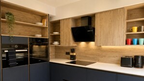A modern kitchen with built-in appliances, wooden shelves, and a black range hood. - East Parade Collection, The Penthouse (North Yorkshire)