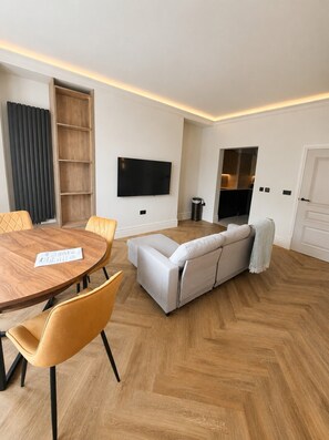 Een moderne woonkamer met een houten eettafel, bank en televisie.