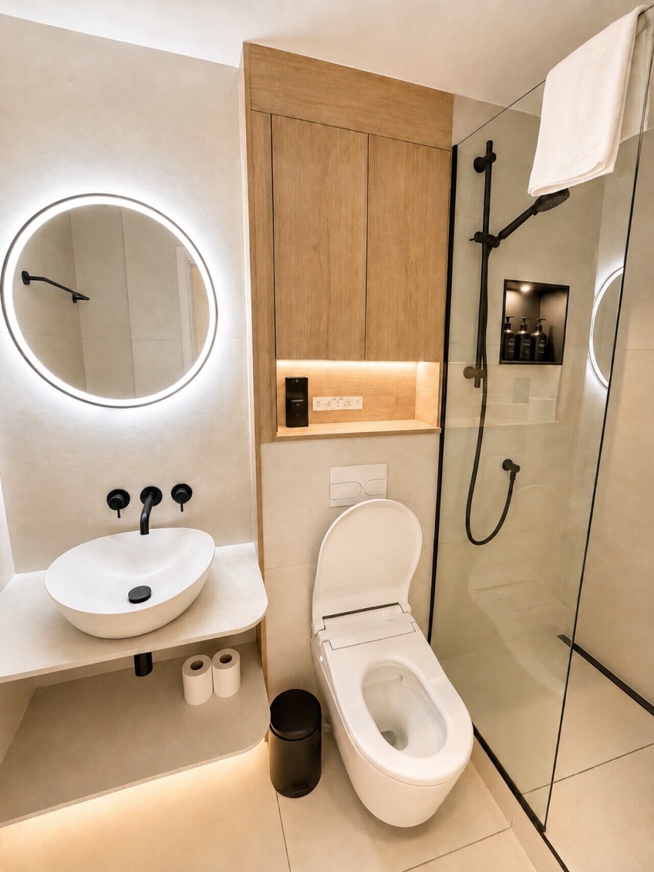 Un bagno moderno con uno specchio rotondo, un lavandino, un water e una cabina doccia in vetro.