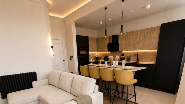 A modern living room with a sectional sofa, a dining area with yellow chairs, and a kitchen with wooden cabinets. - East Parade Collection, Opaz House Flat 3 (North Yorkshire)