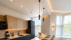 A modern kitchen with a central island, dark cabinetry, and pendant lighting. - East Parade Collection, Opaz House Flat 3 (North Yorkshire)