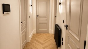 A hallway with a herringbone floor, white walls, and doors with light switch plates. - East Parade Collection, Opaz House Flat 3 (North Yorkshire)