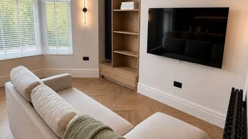 A modern living room with a beige sofa, a flat-screen TV mounted on the wall, and a built-in bookshelf.