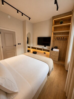 Ein modernes Schlafzimmer mit einem großen Bett, einem Fernseher, einem Holzschrank und einem Spiegel.