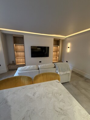 Een moderne woonkamer met een flatscreen televisie, inbouwkasten, een bank en een eethoek met een marmeren tafel.