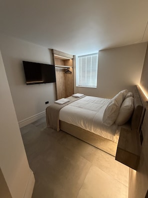 Een slaapkamer met een bed, een aan de muur bevestigde televisie, een raam met zonwering en een inbouwkast.