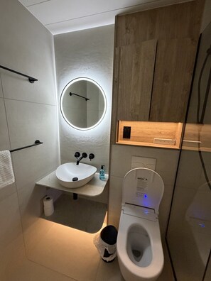 Een moderne badkamer met een wit wastafelmeubel, een ronde spiegel en een toilet.