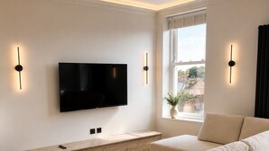 Una sala de estar moderna con un televisor de pantalla plana, una mesa consola de madera, un sofá color beige y una ventana con vistas.