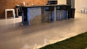 Une cuisine moderne dotée d’un plan de travail en marbre, de tabourets de bar noirs, de luminaires suspendus et d’un réfrigérateur.