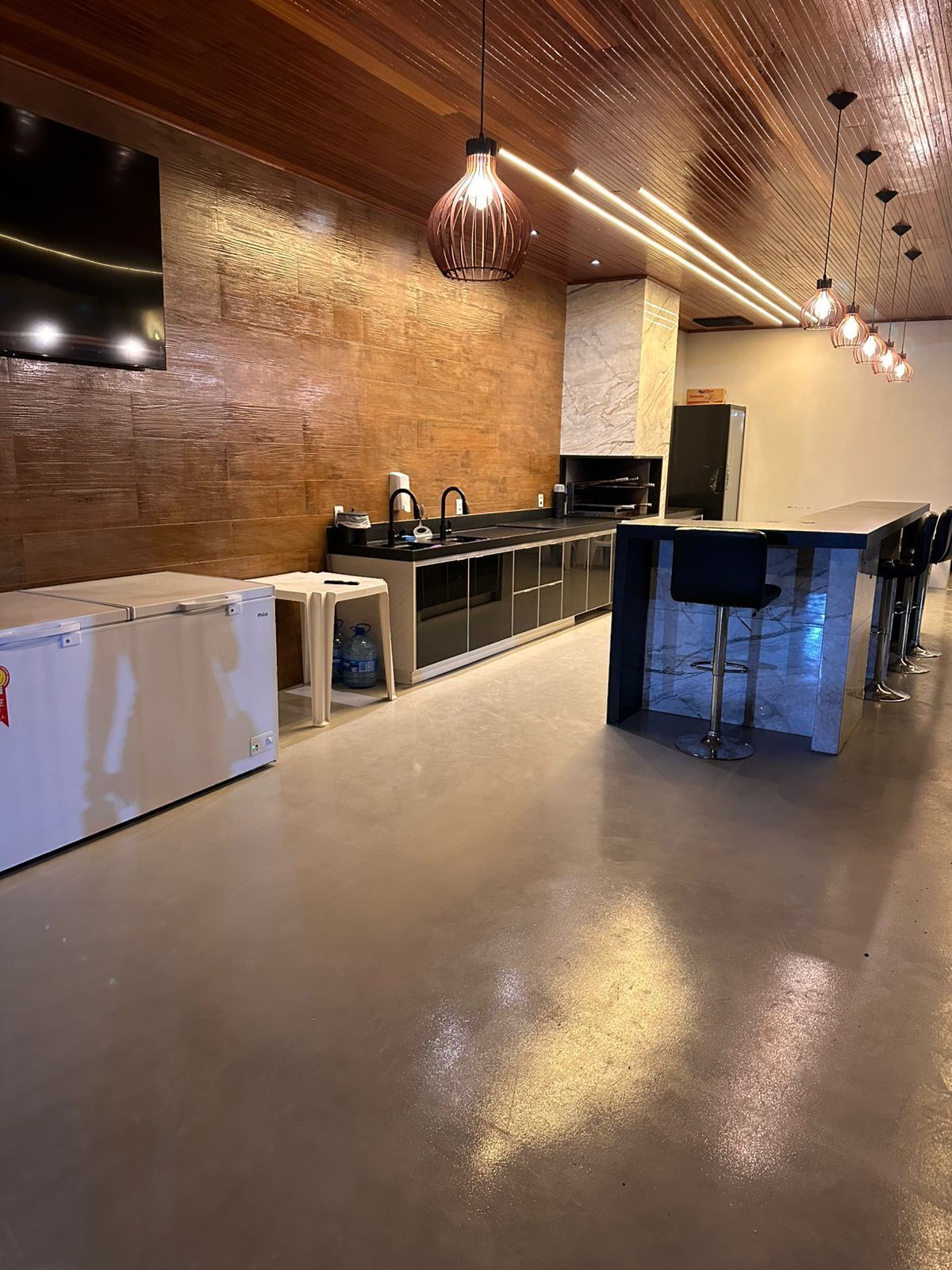 A modern kitchen with a wooden ceiling, a built-in oven, a sink, and a bar area with stools.