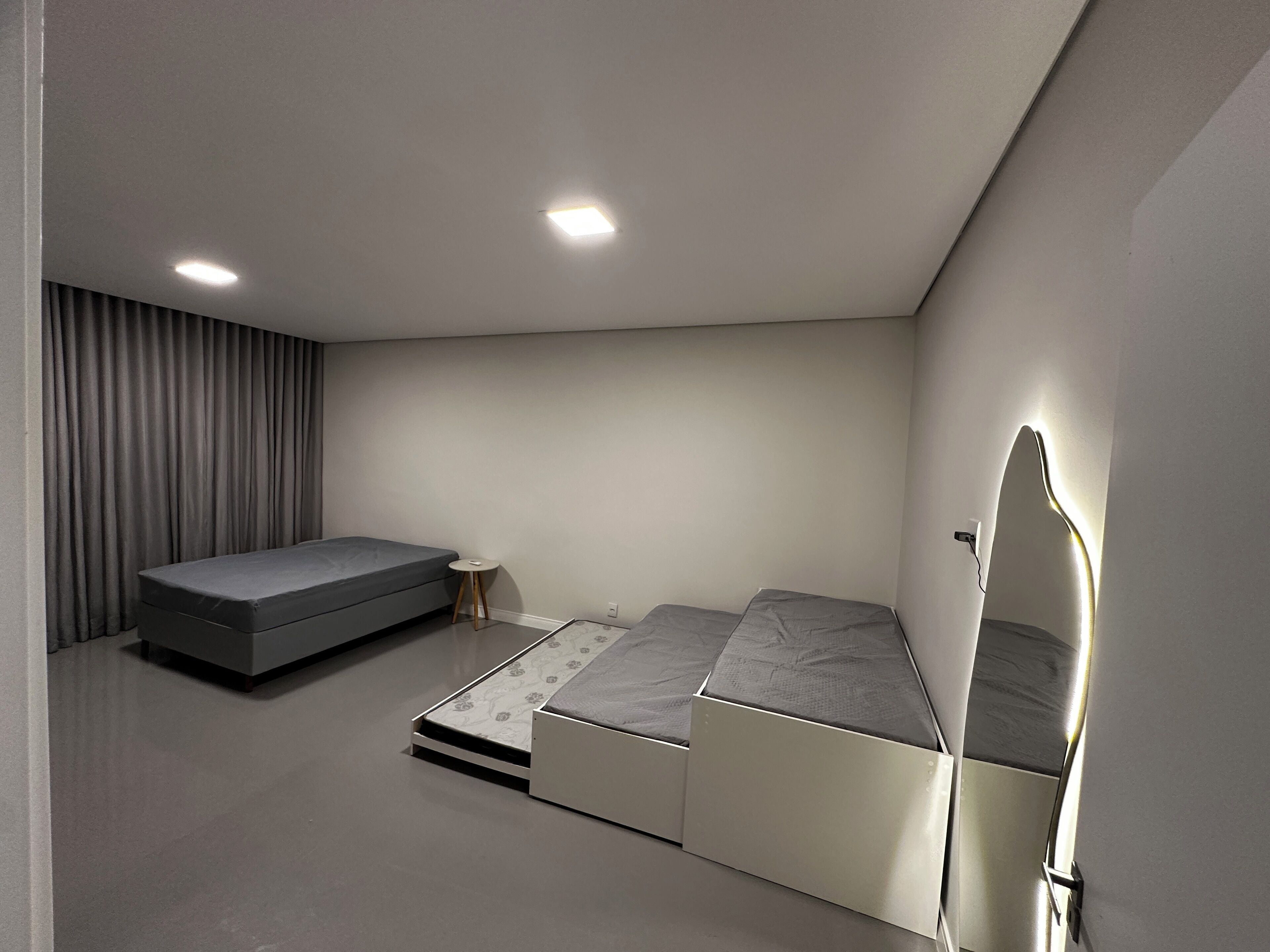 Un dormitorio compacto con una cama, una mesita auxiliar pequeña y un espejo instalado en la pared.